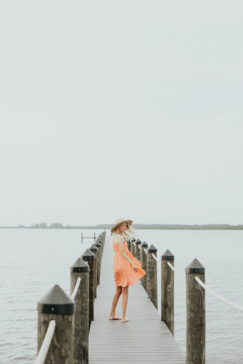 woman in orange spaghetti strap mini dress standing on brown wooden dock during daytime, HD phone wallpaper