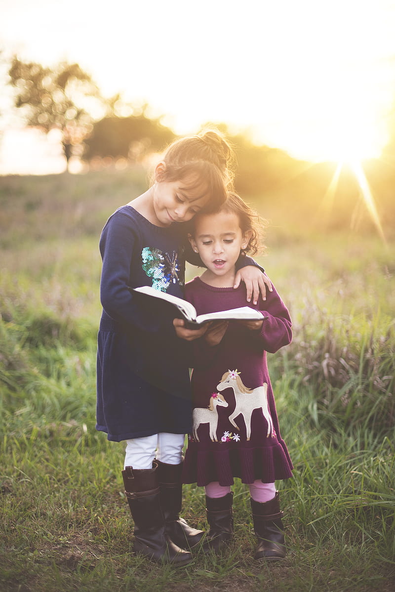 girl's left hand wrap around toddler while reading book during golden hour, HD phone wallpaper