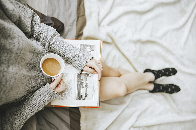 woman holding a cup of coffee at right hand and reading book on her lap while holding it open with her left hand in a well-lit room, HD wallpaper