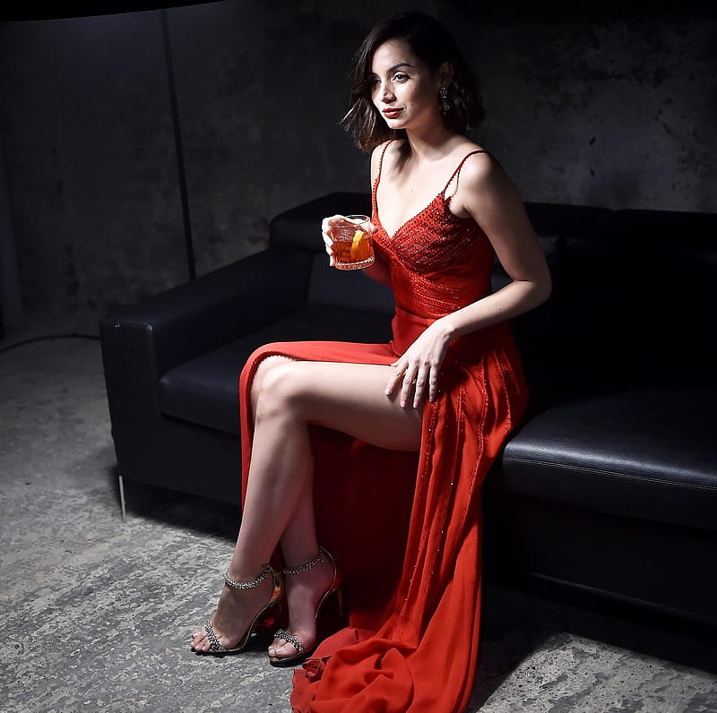 Ana de Amas, spaghetti straps, high heels, brunette, sitting on leather couch, holdng old fahioned glass, long with expoed left thigh, jewelry, red dress, HD wallpaper