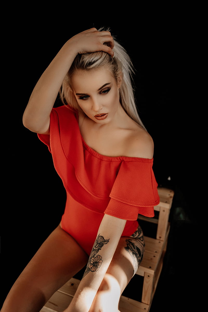 women, model, blonde, long hair, straight hair, dyed hair, looking away, holding hair, touching hair, red clothing, sitting, sunlight, natural light, lipstick, red lipstick, eyeshadow, makeup, mascara, tattoo, bare shoulders, simple background, dark background, black background, vertical, HD phone wallpaper