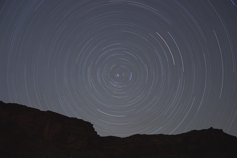 Concentric circles created by stars moving through the night sky over a silhouetted rock face, HD wallpaper