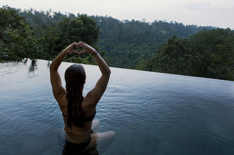 woman in infinity pool making heart hand gesture facing green leafed trees, HD wallpaper