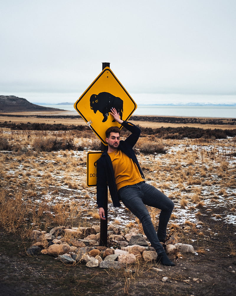 person in black jacket and blue denim jeans sitting on yellow and black road sign during, HD phone wallpaper