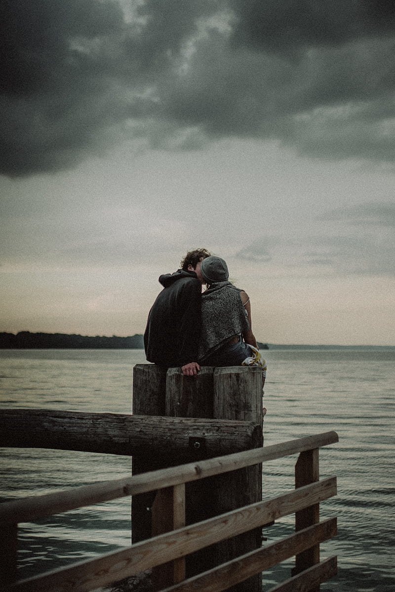 man and woman sitting and kissing on post near the body of water, HD phone wallpaper