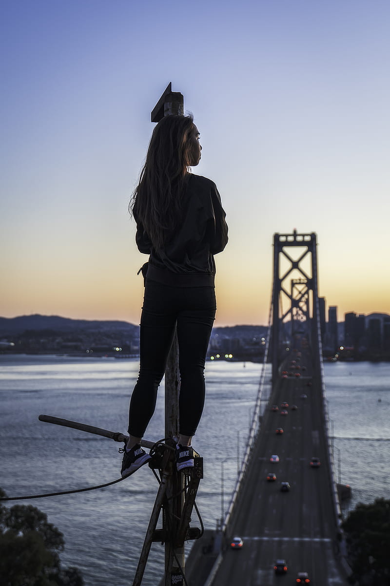 woman standing on metal pole looking at Oakland Bay Bridge during golden hour, HD phone wallpaper