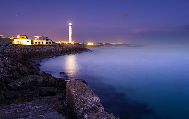 lit lighthouse at a night seashore, rocks, shore, lighthouse, lights, sea, night, HD wallpaper