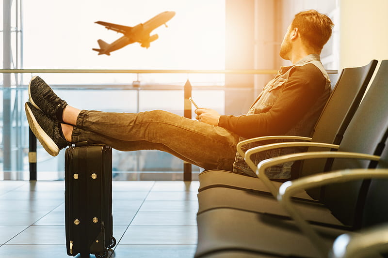 man sitting on gang chair with feet on luggage looking at airplane, HD wallpaper
