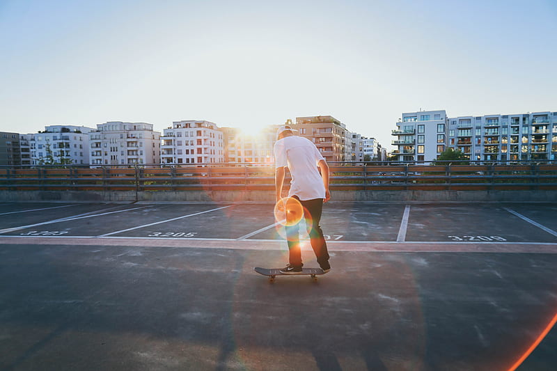 man riding skateboard on parking lot near buildings during golden hour, HD wallpaper