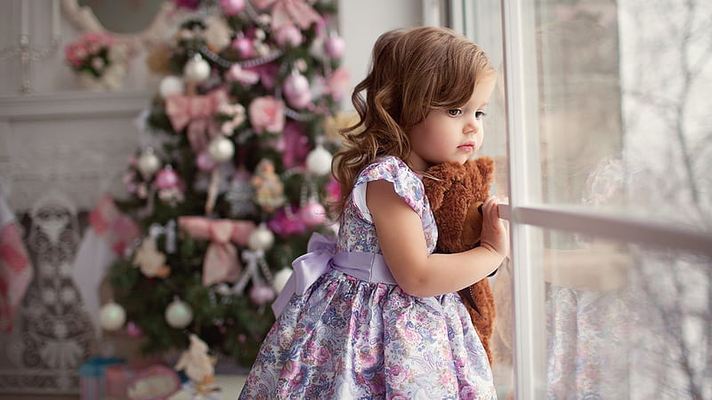 Cute Little Girl With Toy Is Standing Near Glass Window In Blur Decorated Christmas Tree Background Cute, HD wallpaper