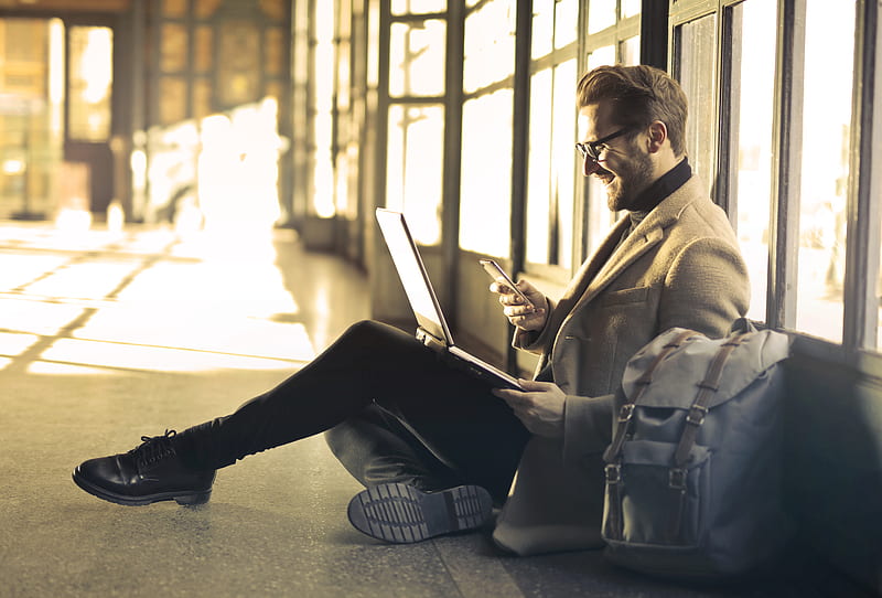 man sitting near window holding phone and laptop, HD wallpaper