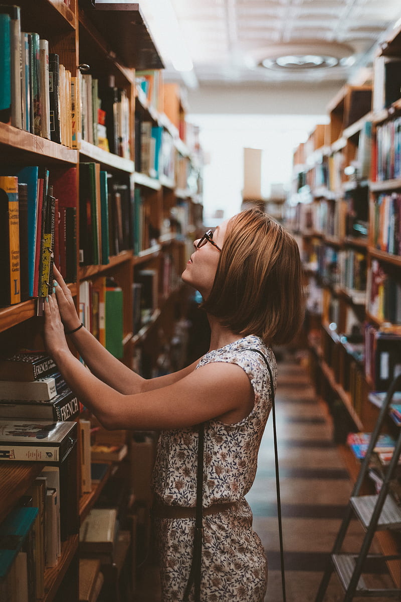 woman standing between library book shelves, HD phone wallpaper