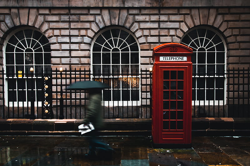 time lapse graphy of woman walking on street while holding umbrella near London telephone booth beside wall, HD wallpaper