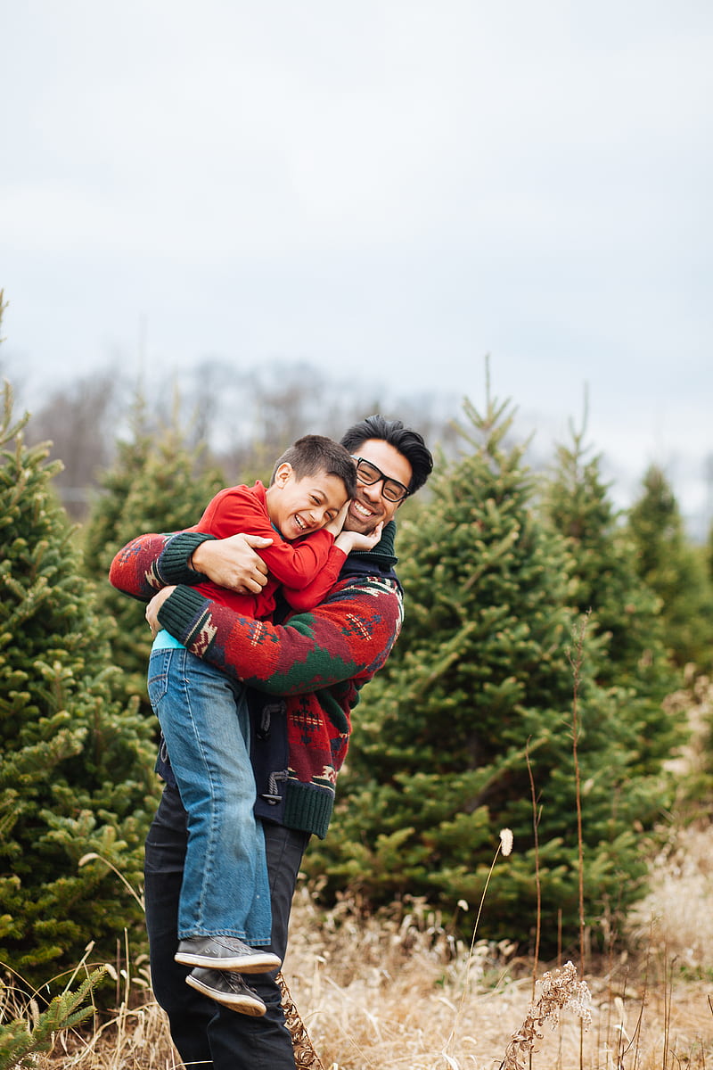 man carrying boy while standing and smiling near pine trees, HD phone wallpaper