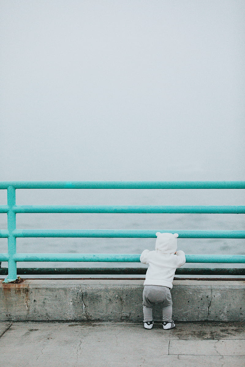 toddler standing while resting arm on rail facing body of water, HD phone wallpaper