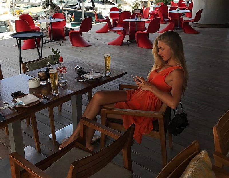 Anjelica Ebbi texting, ash blonde, salmon pink dress, glasses of beer on table, tables and chairs, sitting in open air restaurant, teting on phone, handbag, HD wallpaper