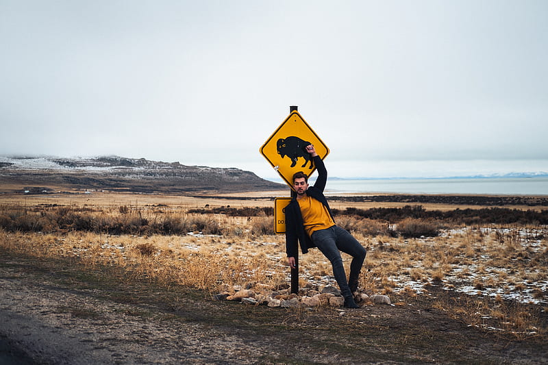 person in black jacket and black pants holding yellow and black road sign, HD wallpaper