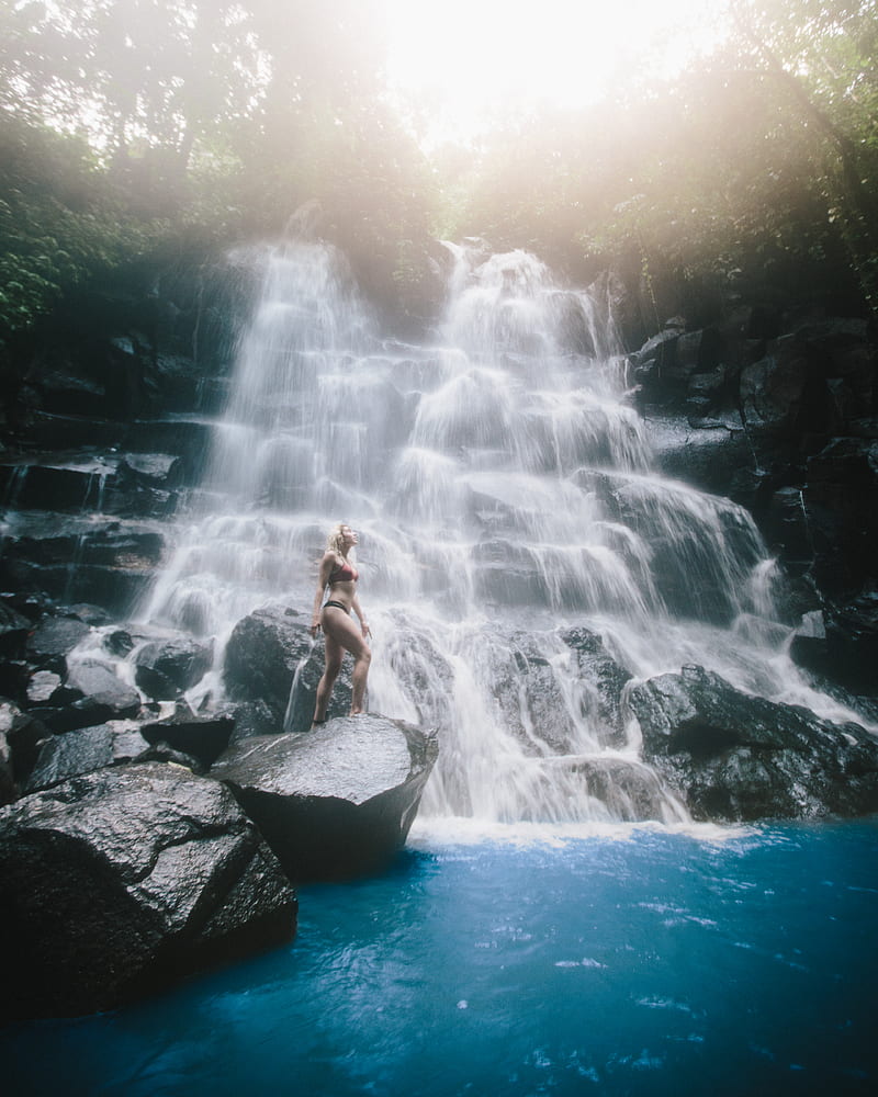 woman standing on rock monolith below waterfall, HD phone wallpaper