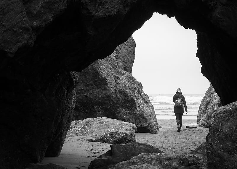 person walking beside rock formation near cave, HD wallpaper