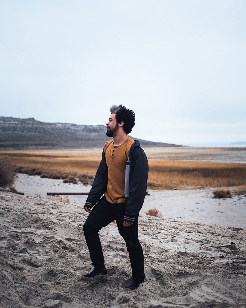 man in brown jacket and black pants standing on gray sand during daytime, HD phone wallpaper