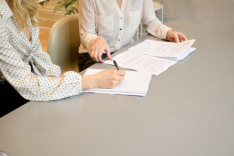 woman signing on white printer paper beside woman about to touch the documents, HD wallpaper