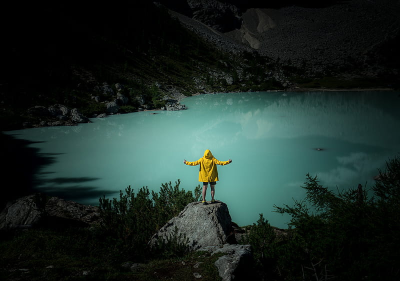 man in yellow jacket and blue denim jeans standing on rock near body of water during, HD wallpaper