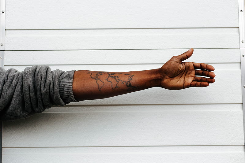 man raising hand with map arm tattoo behind white painted wall, HD wallpaper