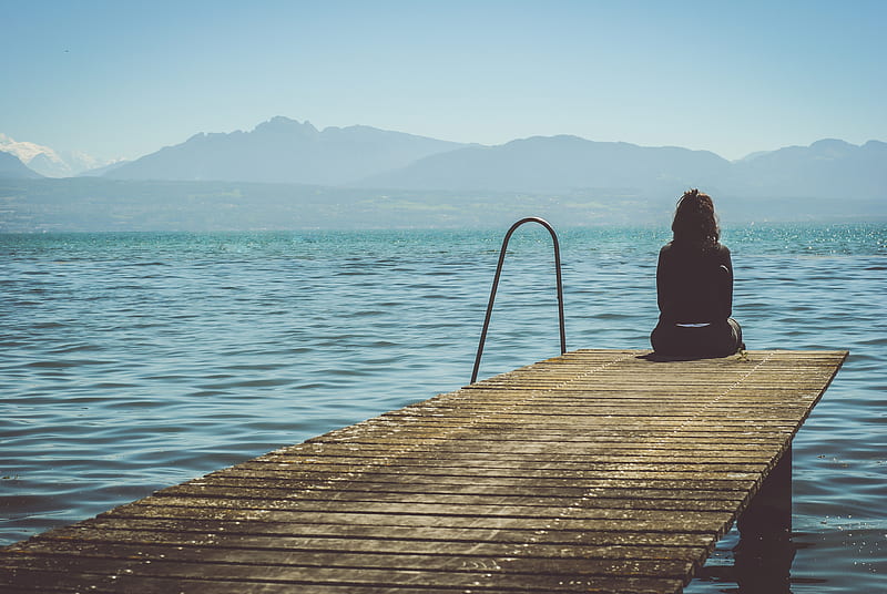 a woman sits on the end of a dock during daytime staring across a lake, HD wallpaper