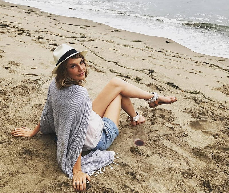 Angela Lindvall on the beach, blue wool, fedora, white t shirt, waves, brunette with red highlights, shawl, denim shorts, wine glass, red wine almost empty, sand, sandals, HD wallpaper