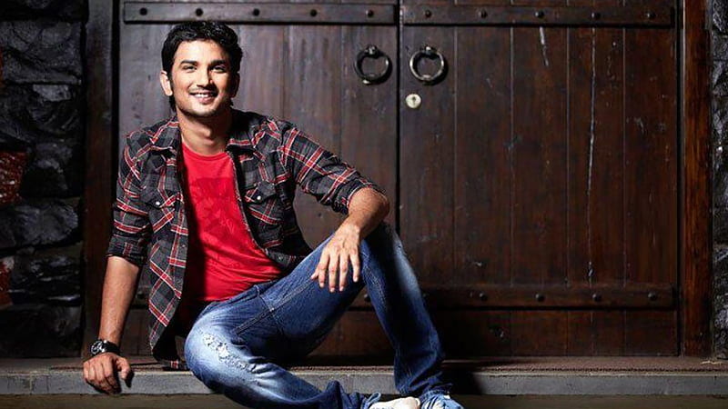Sushant Is Sitting On Floor Wearing Red Black Shirt And Blue Jean In Wooden Door Background Sushant Singh Rajput, HD wallpaper