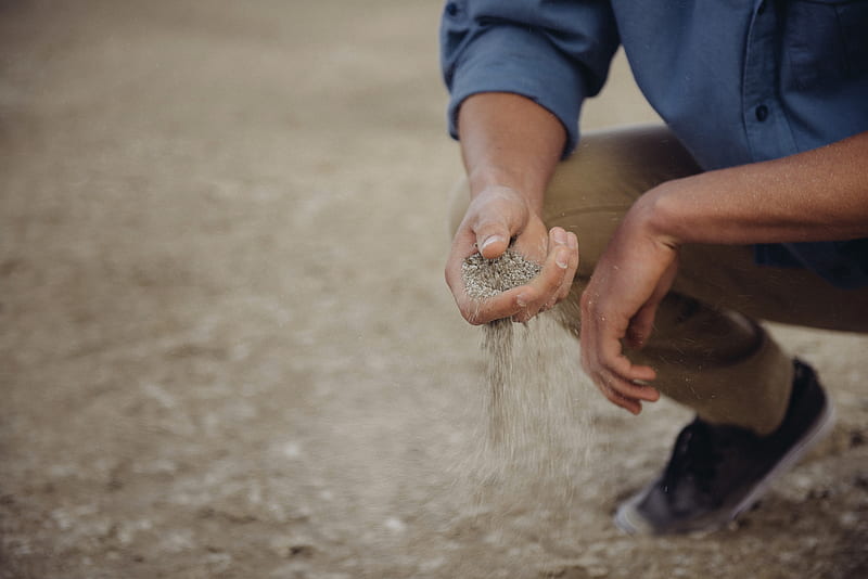 Person crouches down with a handful of sand that slips through their fingers, HD wallpaper
