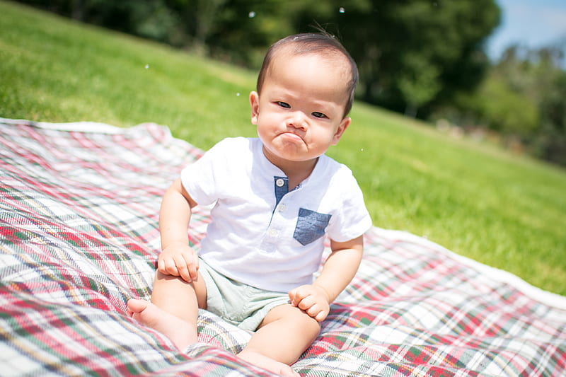 selective focus graphy of grumpy face toddler sitting on plaid pad taken during daytime, HD wallpaper