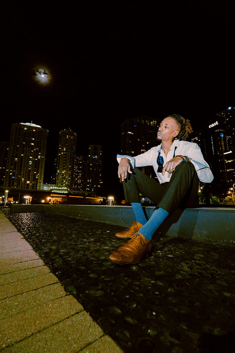 man in white dress shirt and black pants sitting on gray concrete pavement during night time, HD phone wallpaper