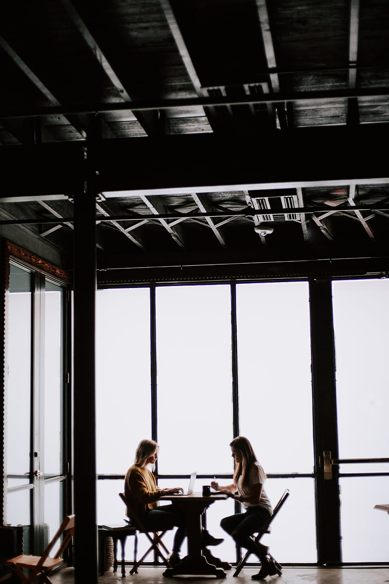 two women facing each other sitting in front of table near glass wall, HD phone wallpaper