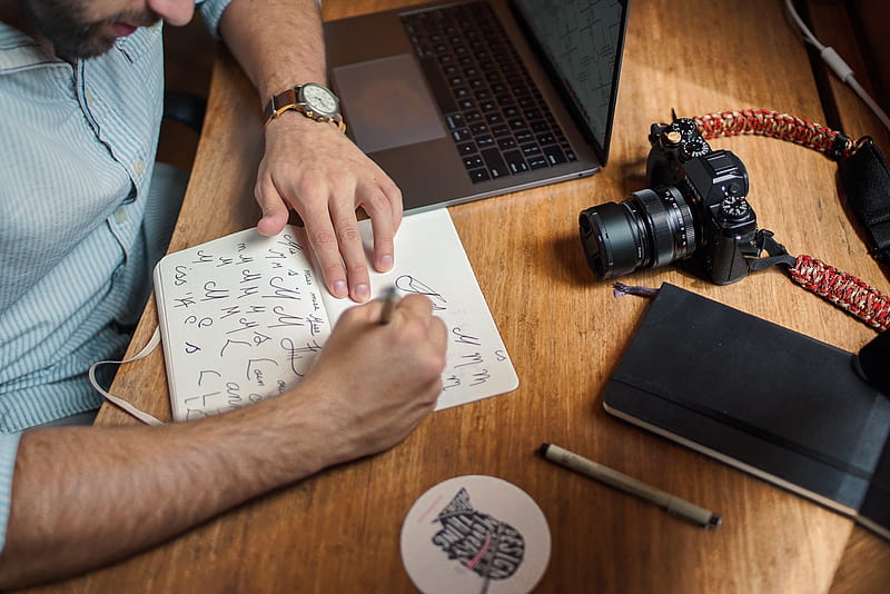 man writing on paper in front of DSLR, HD wallpaper