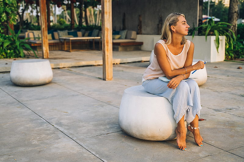 Woman in white tank top and gray leggings sitting on concrete