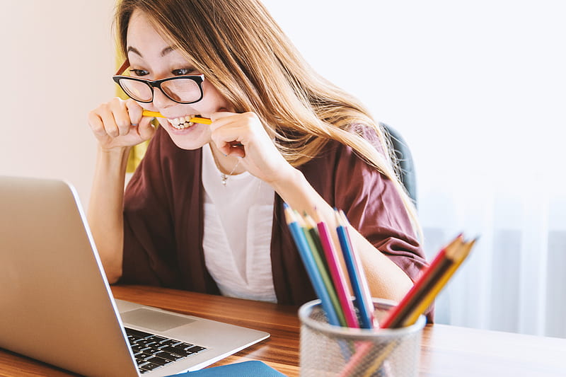 woman biting pencil while sitting on chair in front of computer during daytime, HD wallpaper