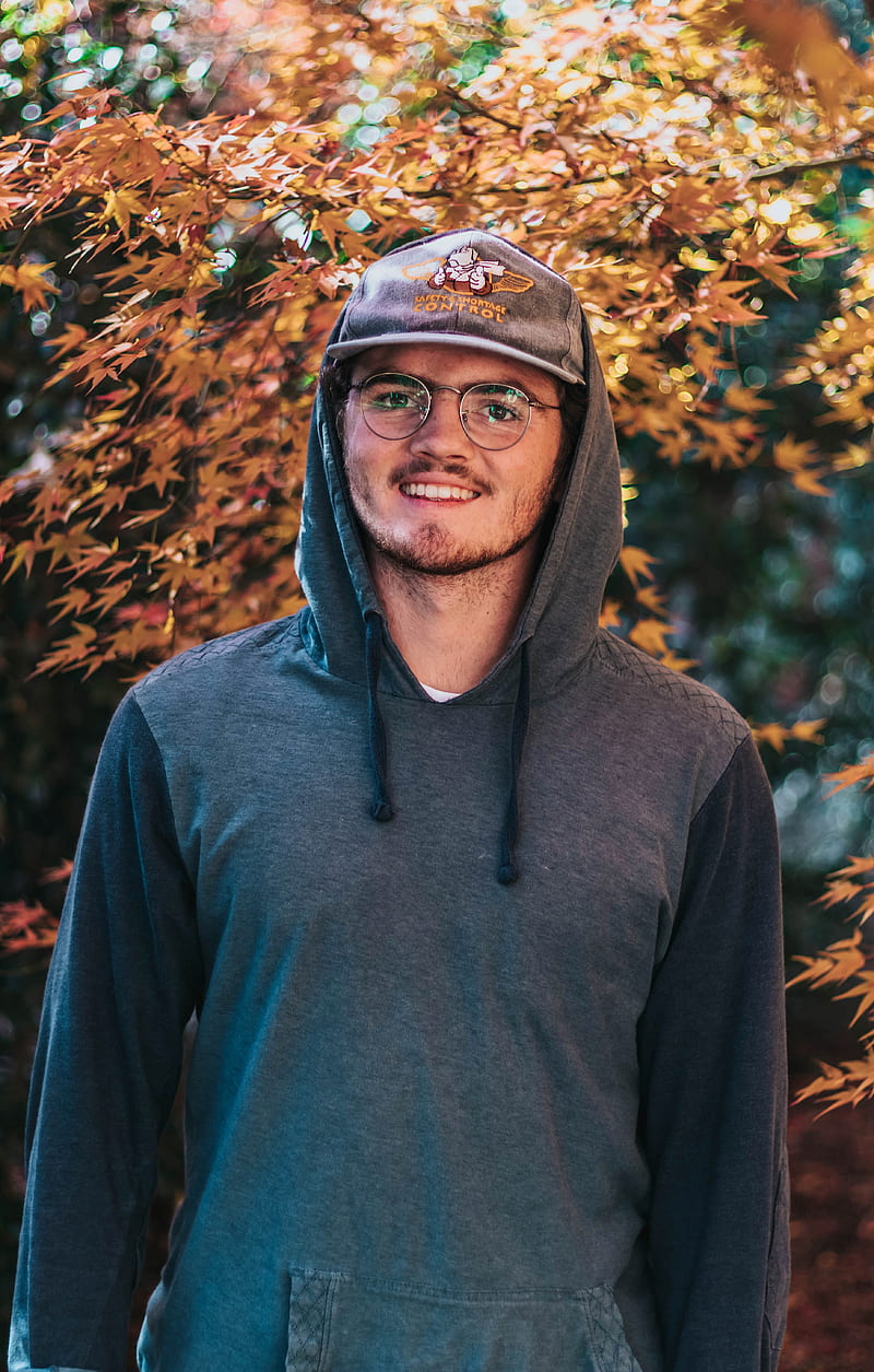 smiling man wearing hoodie and hat near brown tree, HD phone wallpaper
