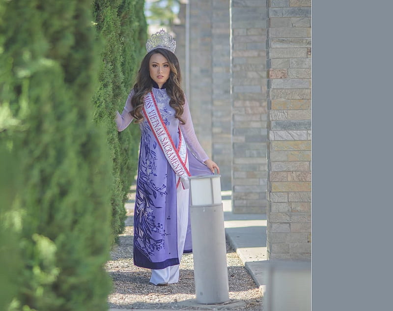 Tracie Dang-Perez, high bushes, brunette, white rob underneath, brick columns, posing in walk way, tiara, traditional clothing, blue with paterns, HD wallpaper