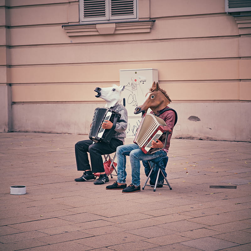two person wearing horse heads sitting on folding chairs while playing accordions beside brown concrete building, HD phone wallpaper