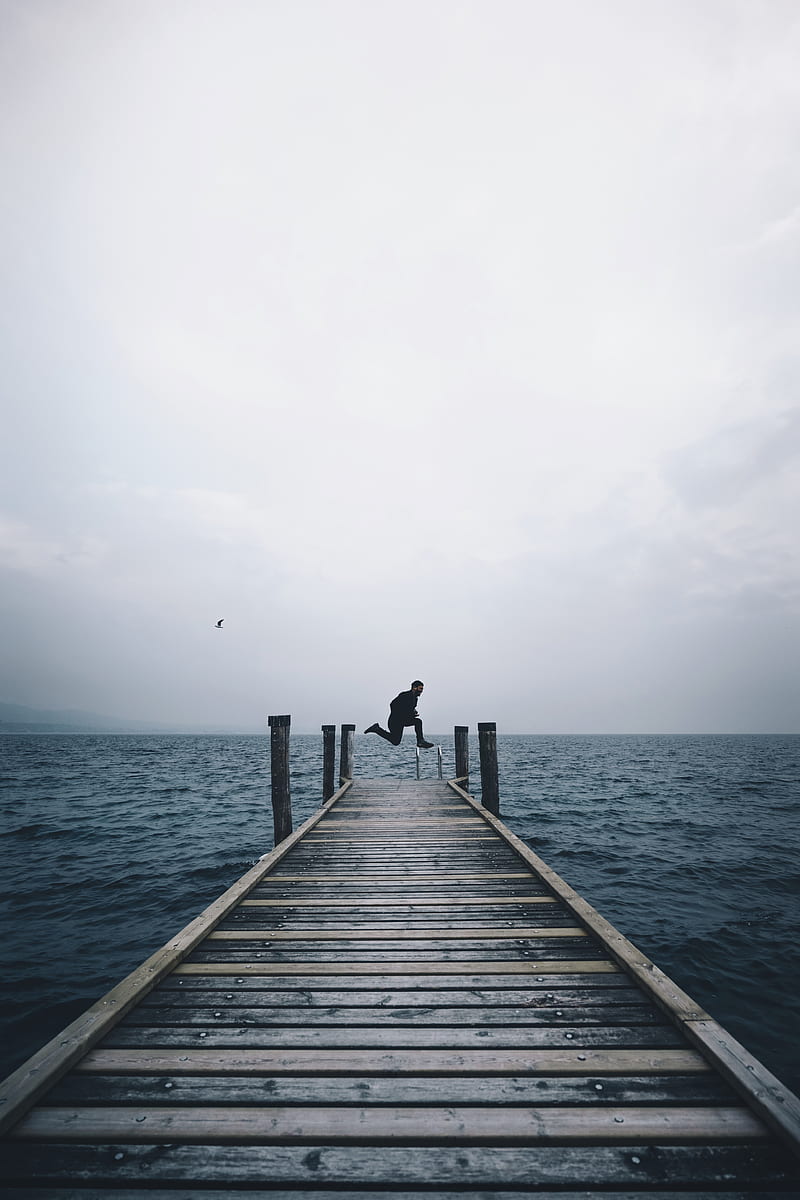 man jumping on brown wooden dock in middle of body of water, HD phone wallpaper