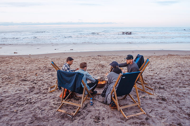 three men and one woman sitting on beach lounge in front fire pit near seashore, HD wallpaper