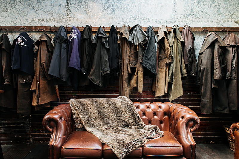 Various outerwear hanging on hooks at wall with in light vintage studio with brown leather sofa with soft plaid, HD wallpaper