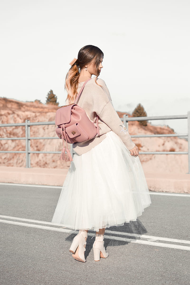 woman standing in front of metal railings wearing brown sweater and white skirt and pair of heeled sandals carrying brown leather backpack during daytime, HD phone wallpaper
