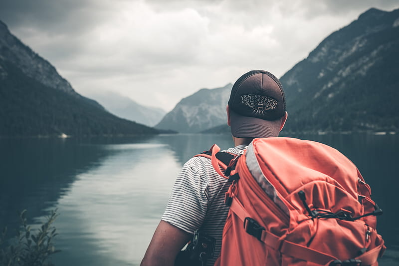 man with red hiking backpack facing body of water and mountains at daytime, HD wallpaper
