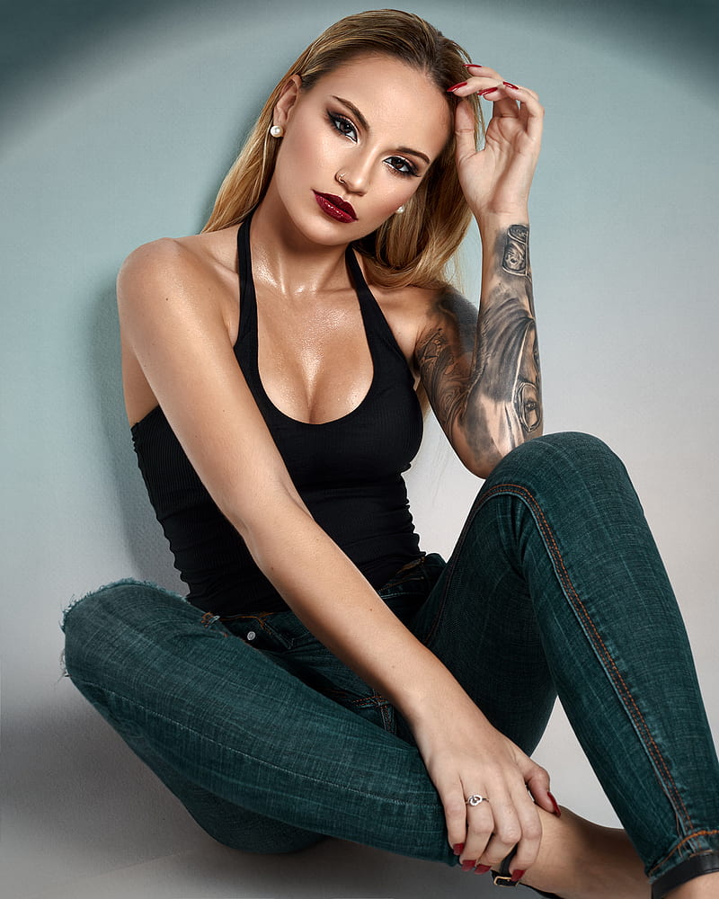 Javier Ullastres, women, blonde, long hair, straight hair, jewelry, earring, beads, painted nails, red nails, long nails, eyeshadow, eyeliner, lipstick, lip gloss, piercing, pierced nose, looking at viewer, tank top, black clothing, cleavage, jeans, denim, rings, tattoo, wall, sweat, body oil, makeup, HD phone wallpaper