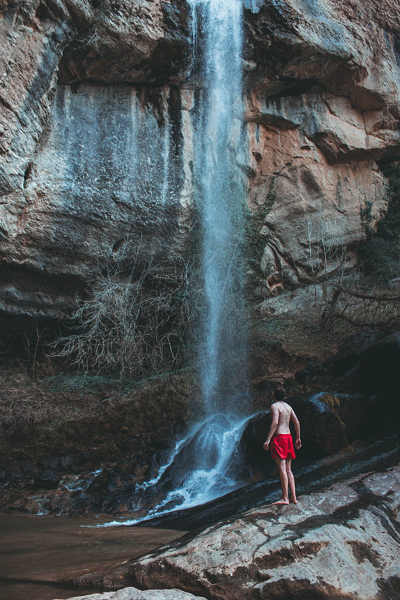 woman in red tank top and black pants standing on rock formation near waterfalls during daytime, HD phone wallpaper