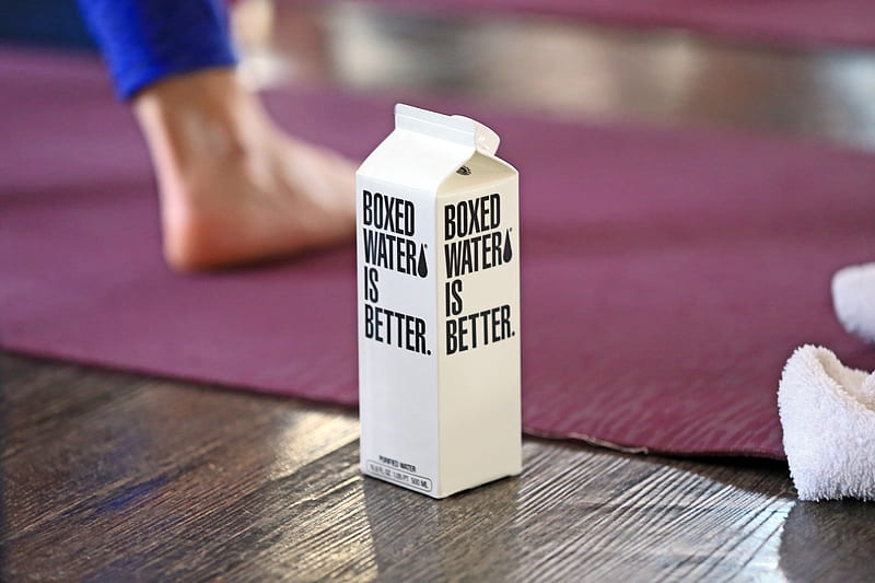 A Boxed Water carton in the foreground with a woman doing yoga in the background, HD wallpaper