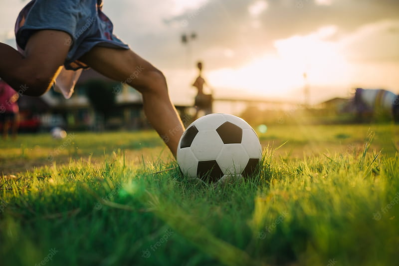 Premium . Boy kicking a ball with bare foot while playing street soccer football on the green grass field, HD wallpaper
